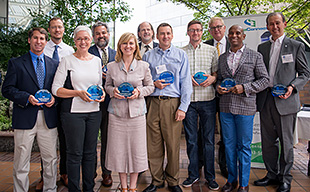 Photo showing a group of men and women holding circular blue awards.