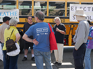 A photo of a group of people talking in front of a school bus.