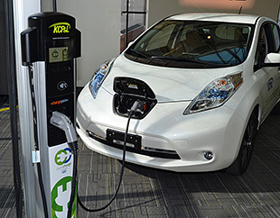 A photo of a white PEV plugged into a charging station.