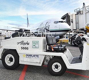 Photo of a white Alaska Air Group Charlatte America eGSE belt loader in front of a white Alaska Air plane.