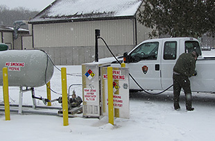 A photo of a man filling a pickup truck with propane in the snow.