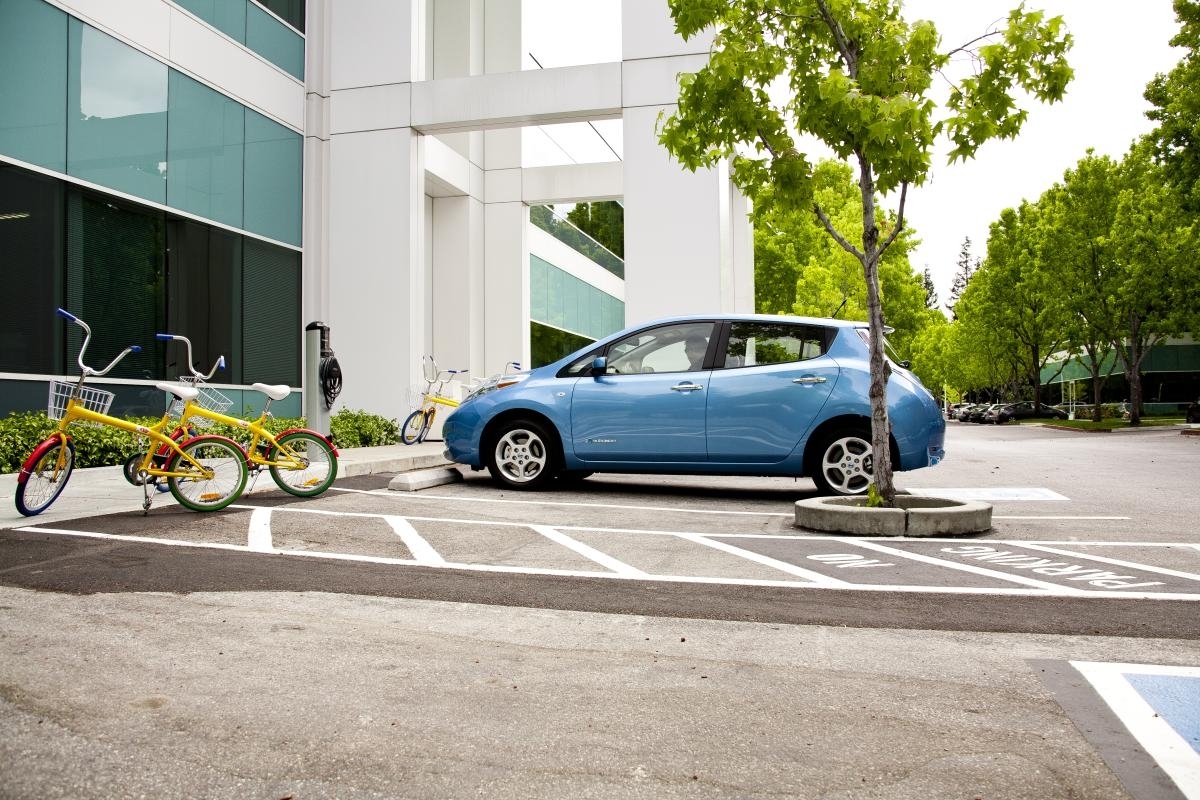 Photo of a Nissan Leaf in a parking lot with access to electric vehicle charging equipment.